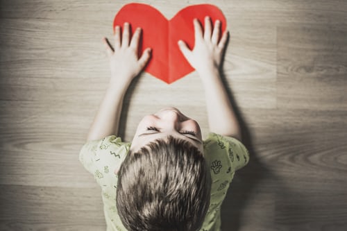 little-boy-on-ground-with-red-paper-heart-happy