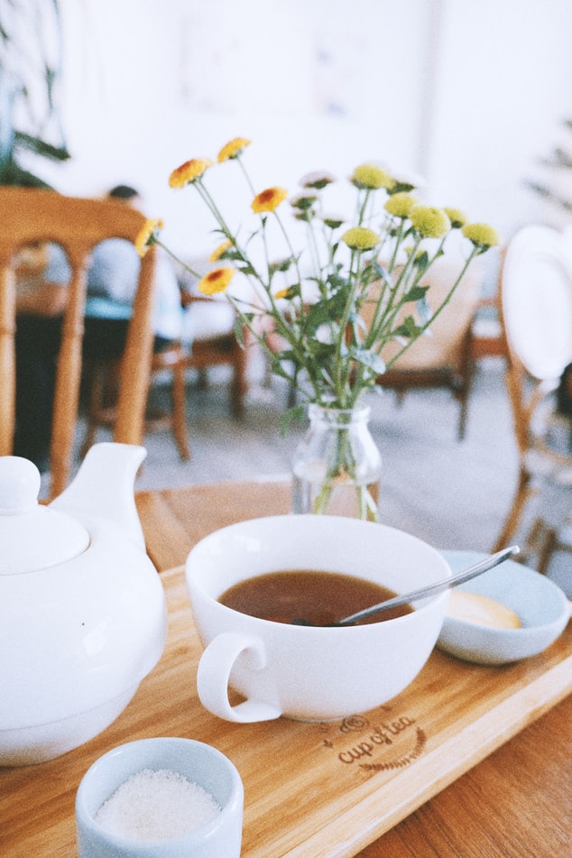 white-cup-of-tea-on-wooden-board-with-sugar-and-flowers